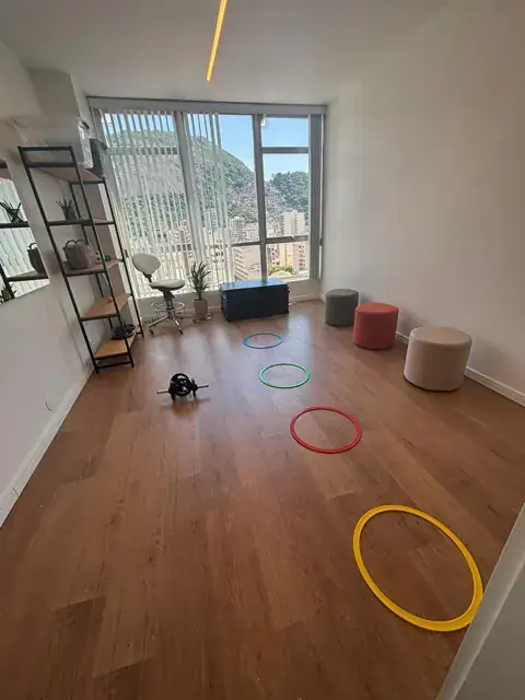 Sala de atividades com bambolês coloridos no chão, pufes e vista para o morro