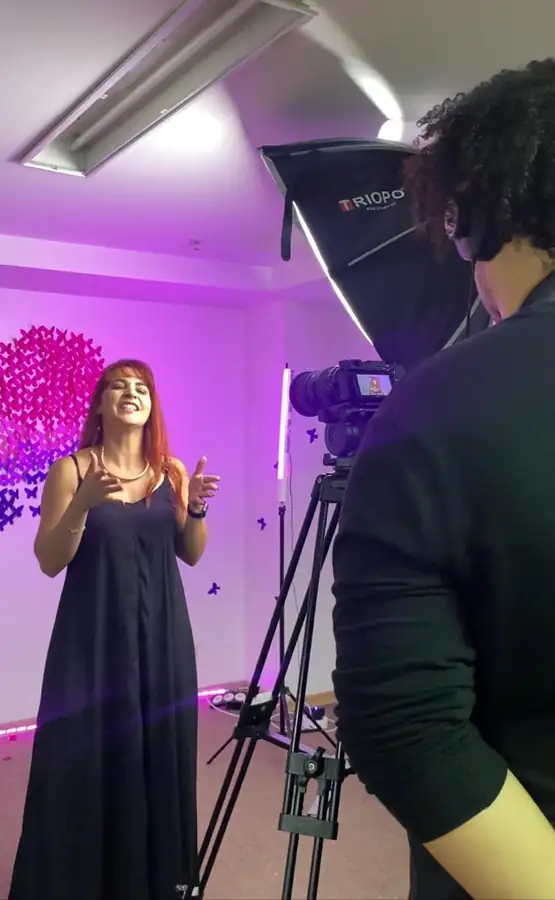 Ana Paula Barbosa gravando conteúdo diante da câmera, em estúdio com iluminação lilás